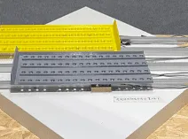 A display of two perforated metal ramps, one gray and one yellow, positioned on a white platform with a label in front of them.