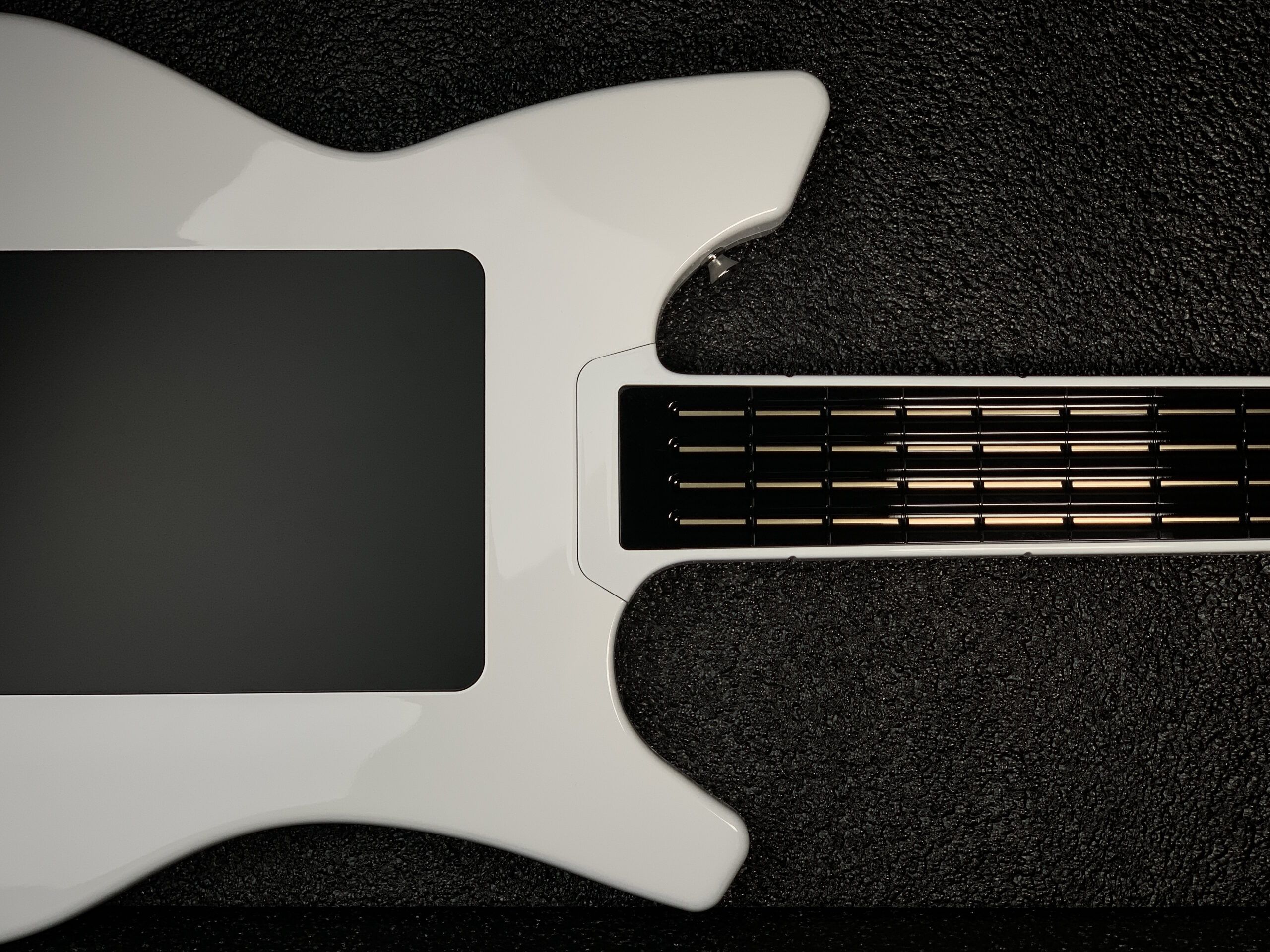A close-up of a modern electric guitar with a glossy white body and a black fretboard, set against a textured black background. The image shows the body and part of the neck.