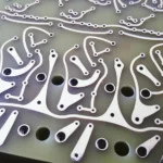 Close-up view of a printed circuit board (PCB) with intricate metallic traces and patterns on a green surface, featuring multiple holes and detailed pathways for electronic components.