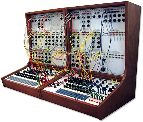 A large modular synthesizer with wooden casing, featuring many colorful patch cables, knobs, buttons, and touchplates, arranged across two angled control panels.