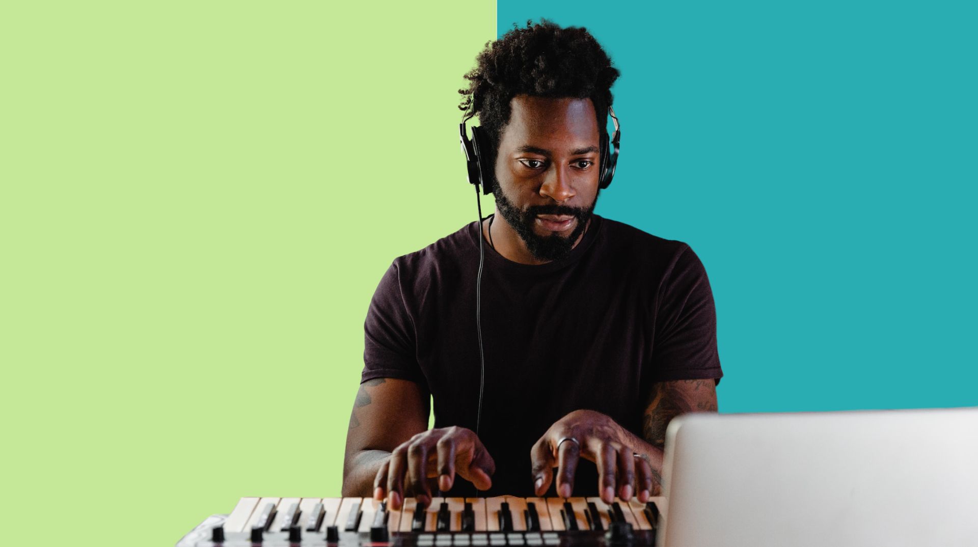 A man wearing headphones is playing a keyboard in front of a laptop. The background features two solid color panels, one green and one teal, creating a vibrant atmosphere.