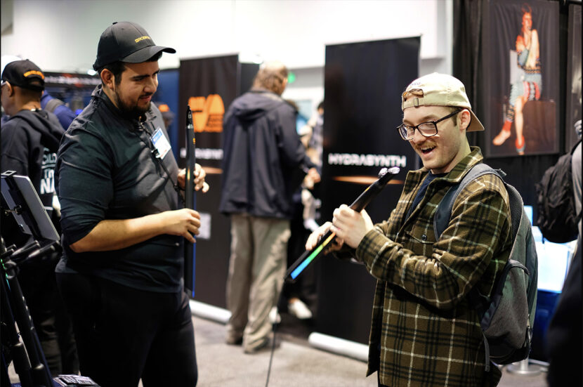 Man playing a wind instrument in front of small gathering at a tradeshow.