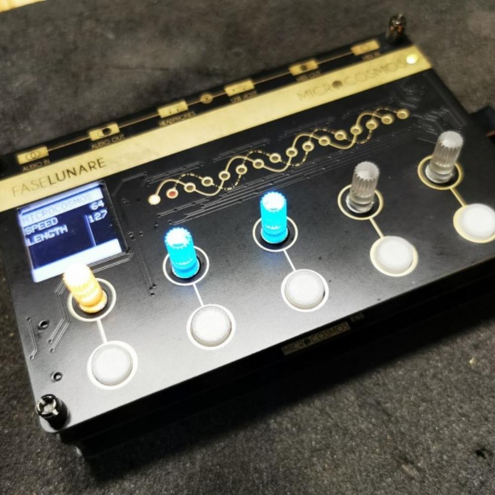 A black electronic music device called Faselunare Microcosmos with four glowing knobs, two blue and two white, and a small screen displaying speed and length settings. The device is placed on a dark surface.