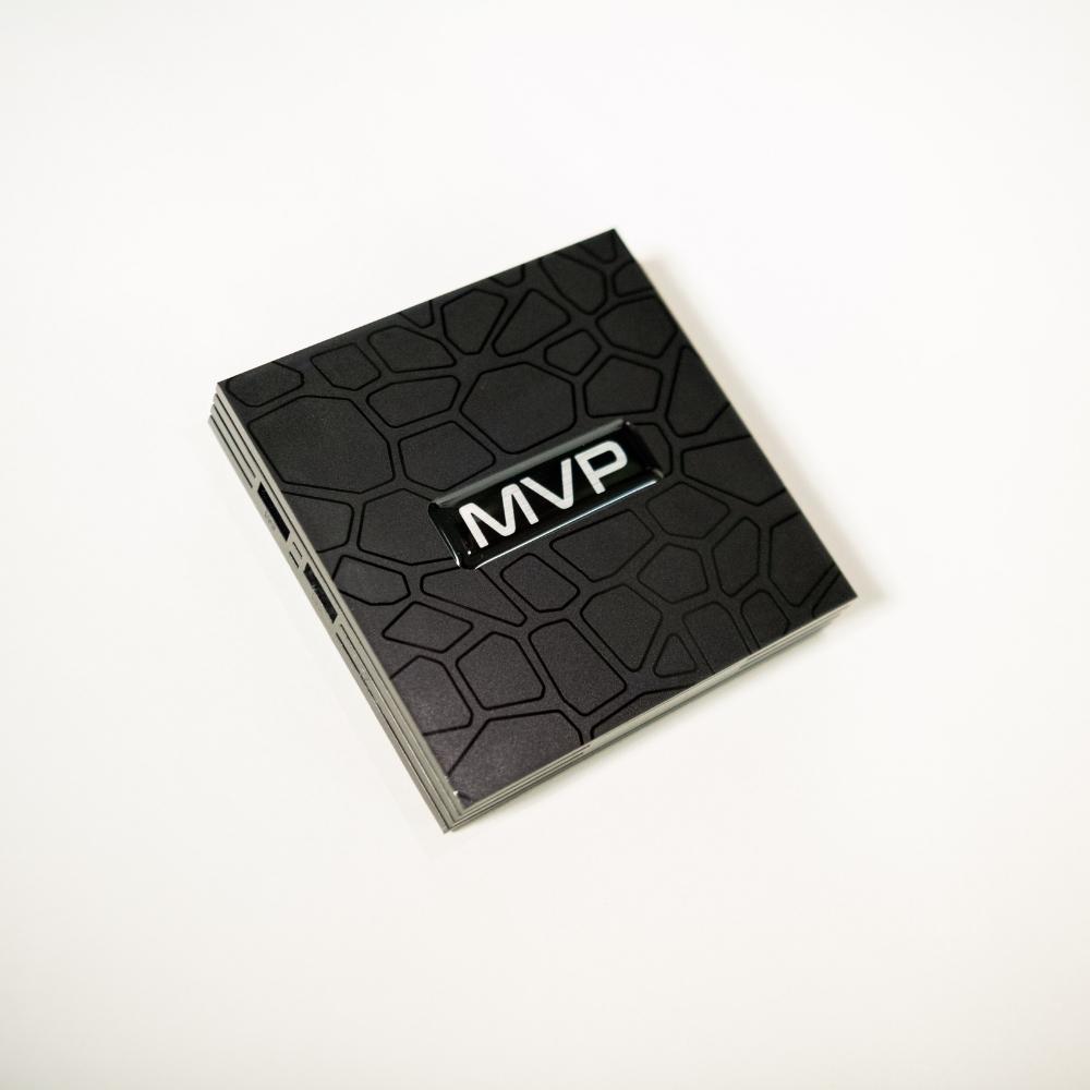 A black, square electronic device with a textured, geometric pattern on the surface and the letters MVP displayed in the center, photographed against a white background.