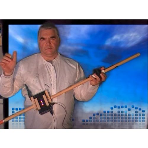 A man in a white shirt stands in front of a blue digital background, holding an electronic musical instrument made of wood with attached electronic components.