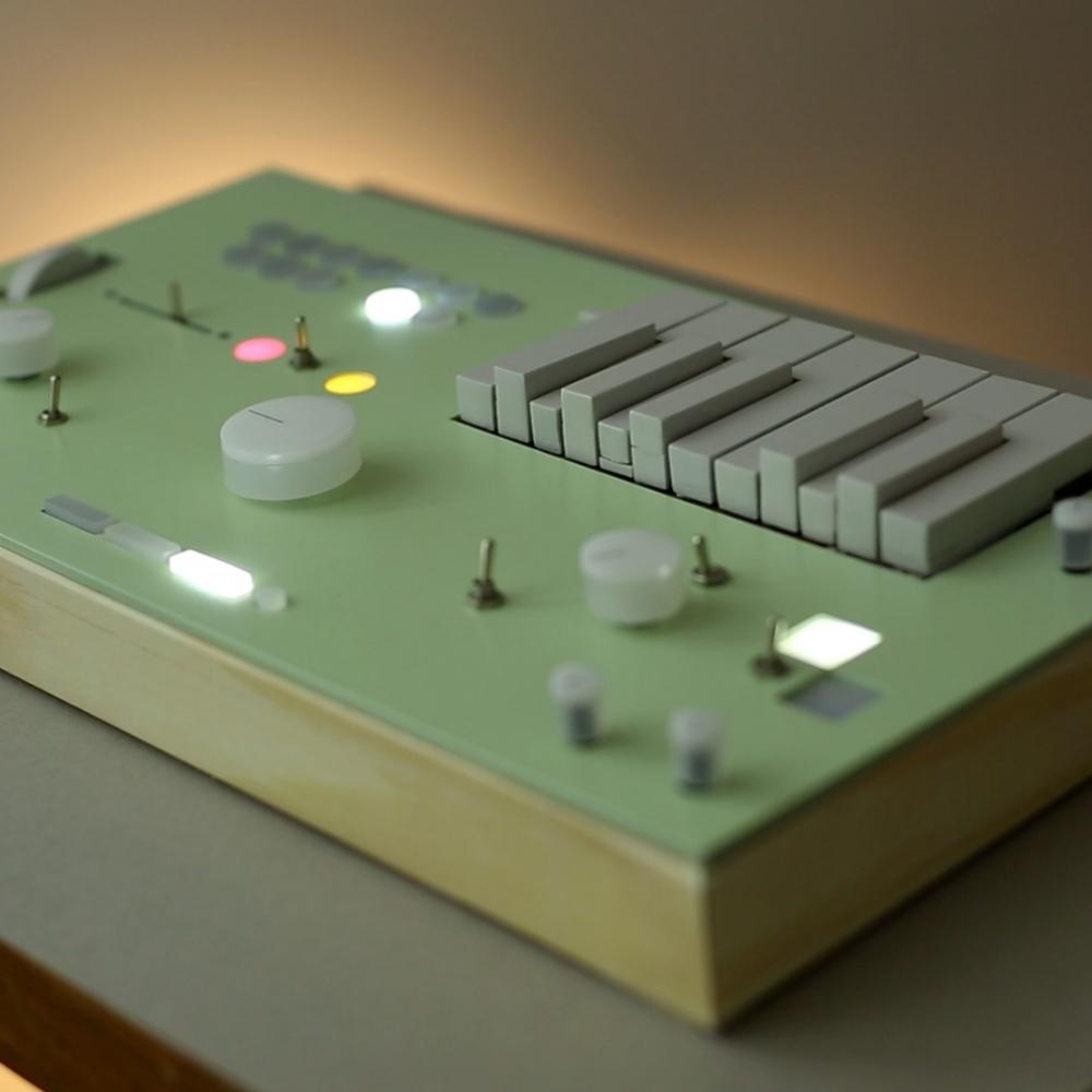 A minimalist electronic music synthesizer with white knobs, sliders, switches, and rectangular keys on a light green panel with a wooden base, softly lit from the side.