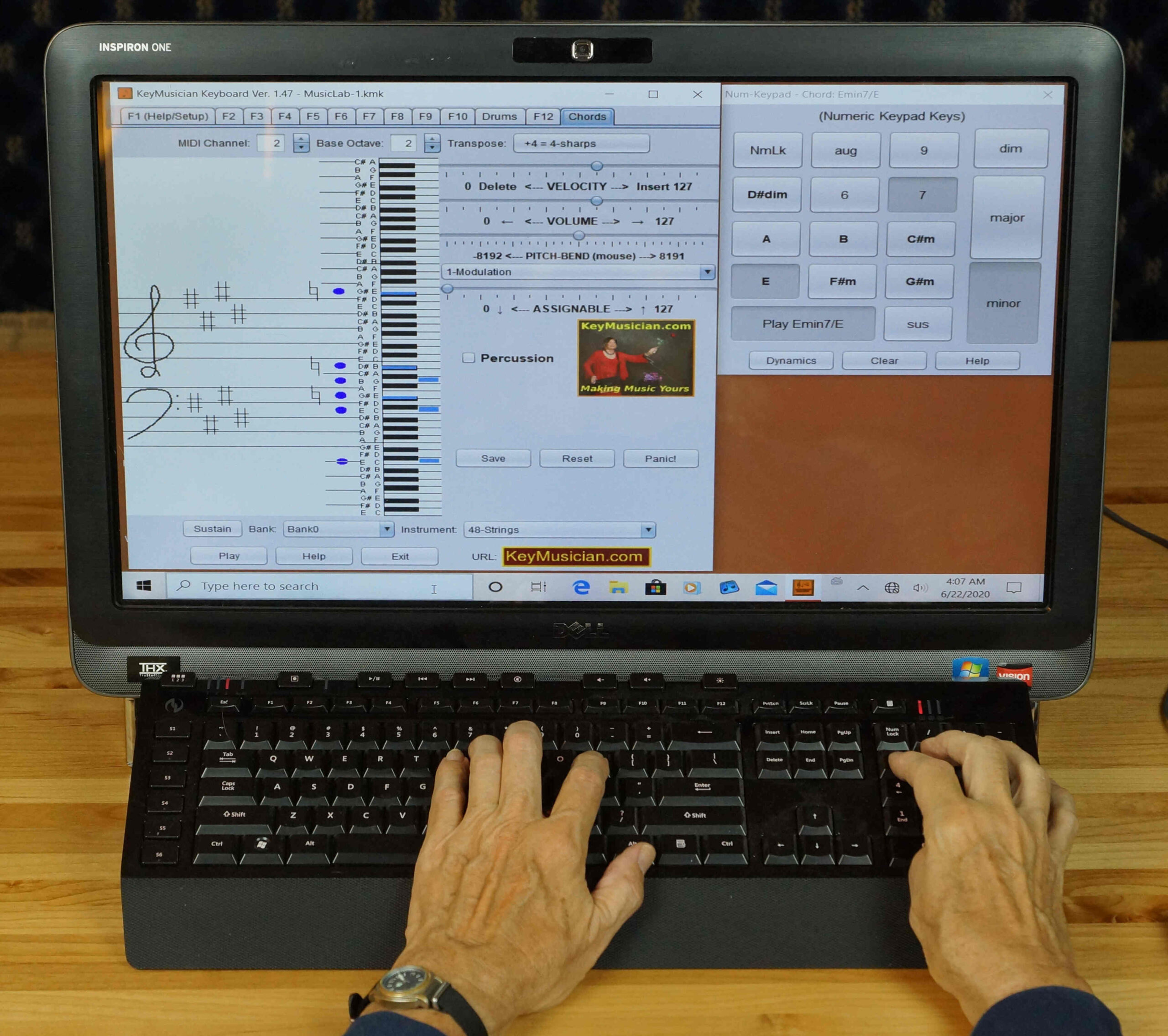 A person uses both the keyboard and touch screen of a large computer displaying a virtual musical keyboard interface with musical notes and chord options.