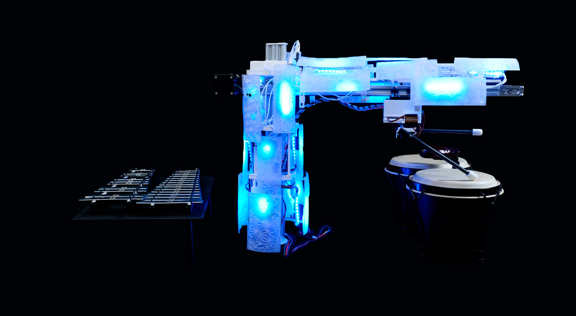 A robotic arm with glowing blue lights is positioned between a metal xylophone on the left and two conga drums on the right, set against a black background.