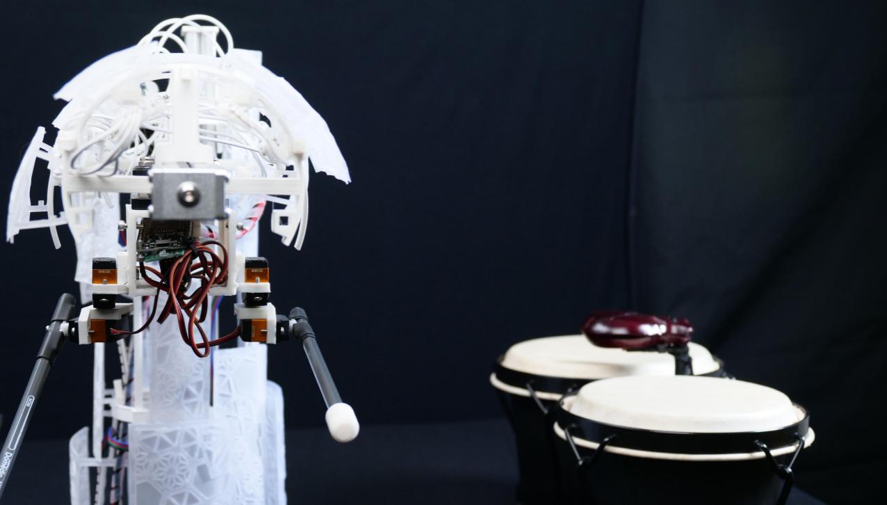 A white, partially transparent robot with wires exposed extends an arm toward two bongo drums set against a black background.
