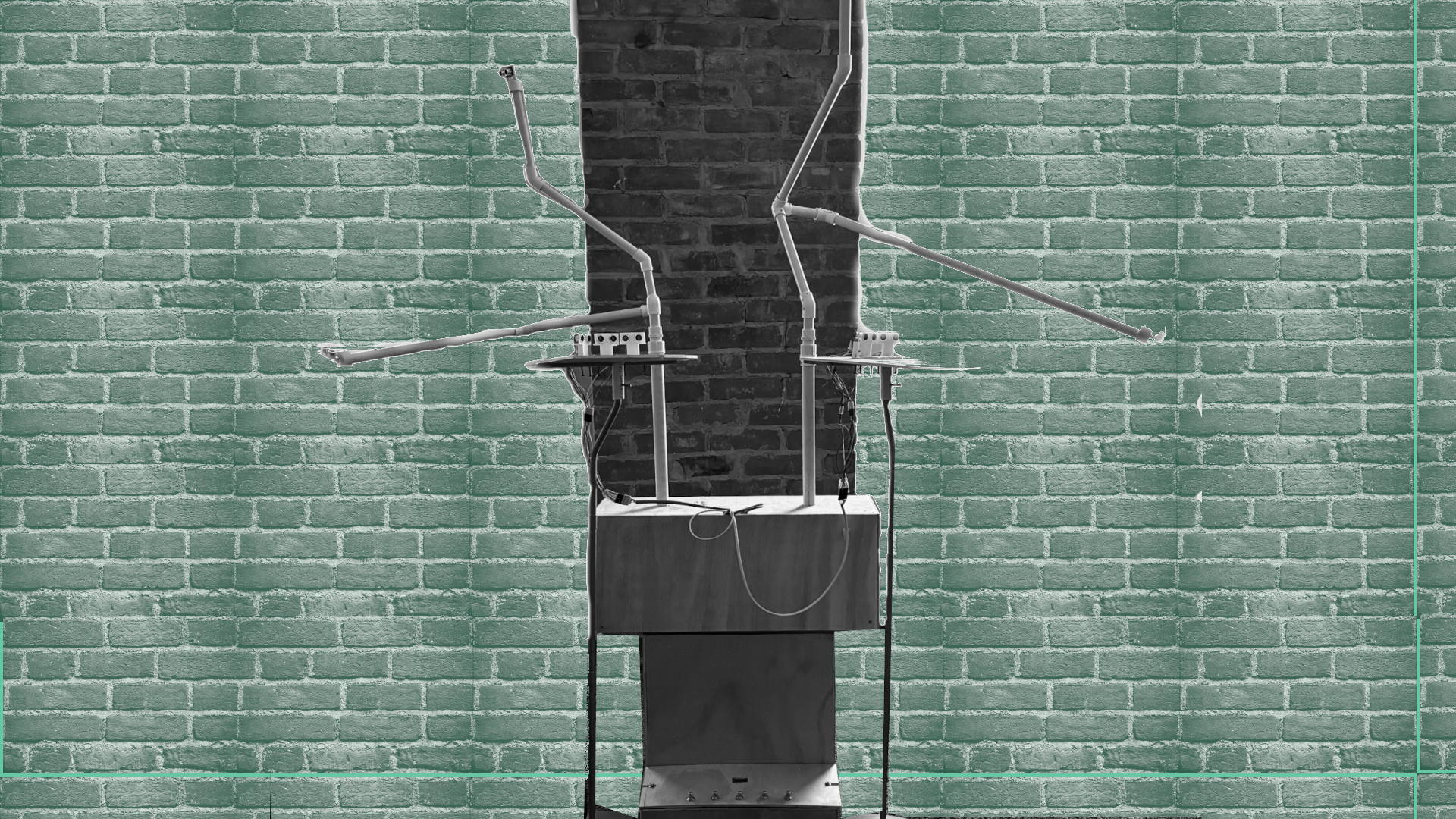A metal stand with thin, bent metal rods and attached wires stands against a teal brick wall with a vertical black stripe in the center. The structure has a small box at its base.