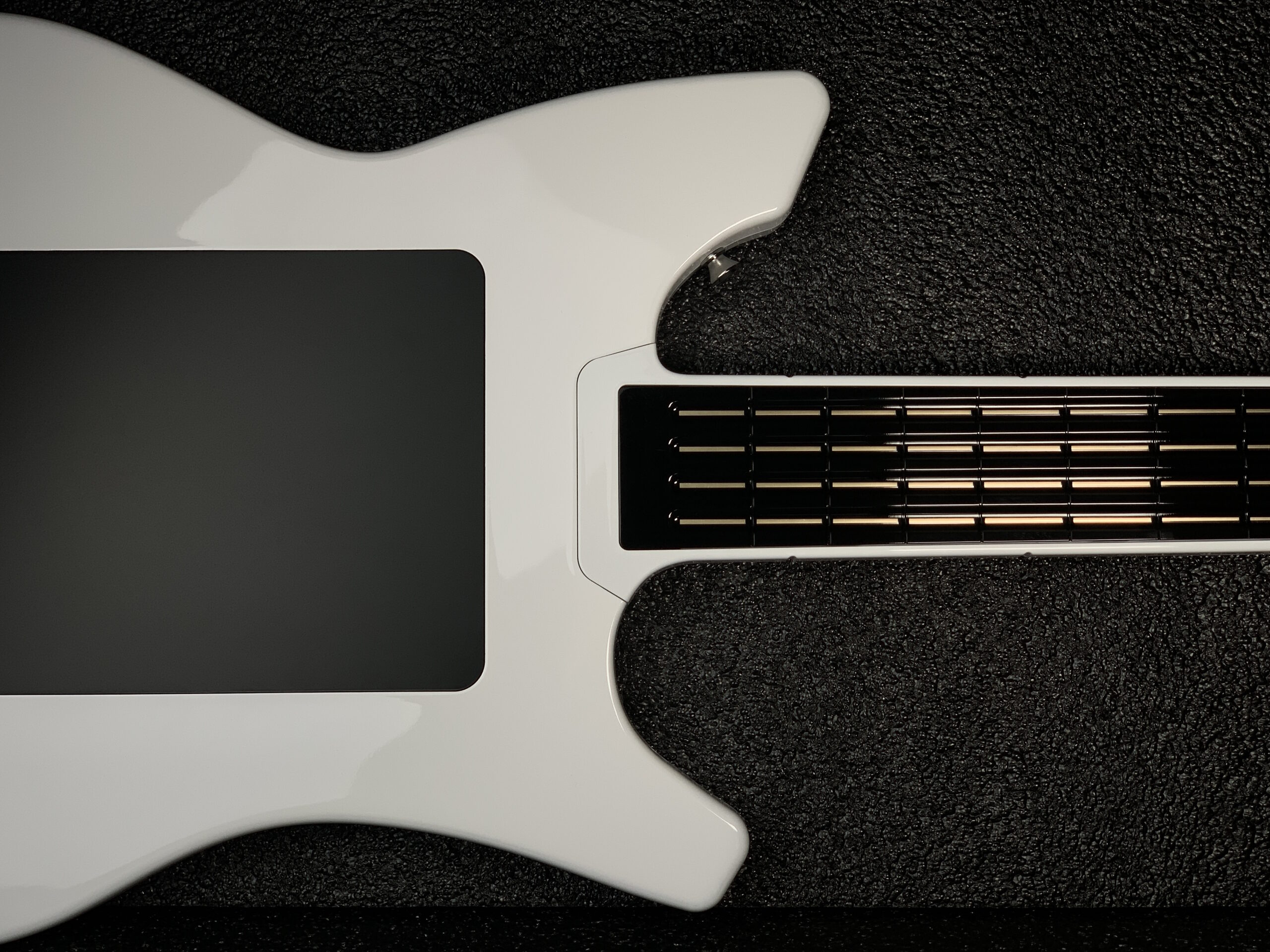 A close-up of a modern electric guitar with a glossy white body and a black fretboard, set against a textured black background. The image shows the body and part of the neck.