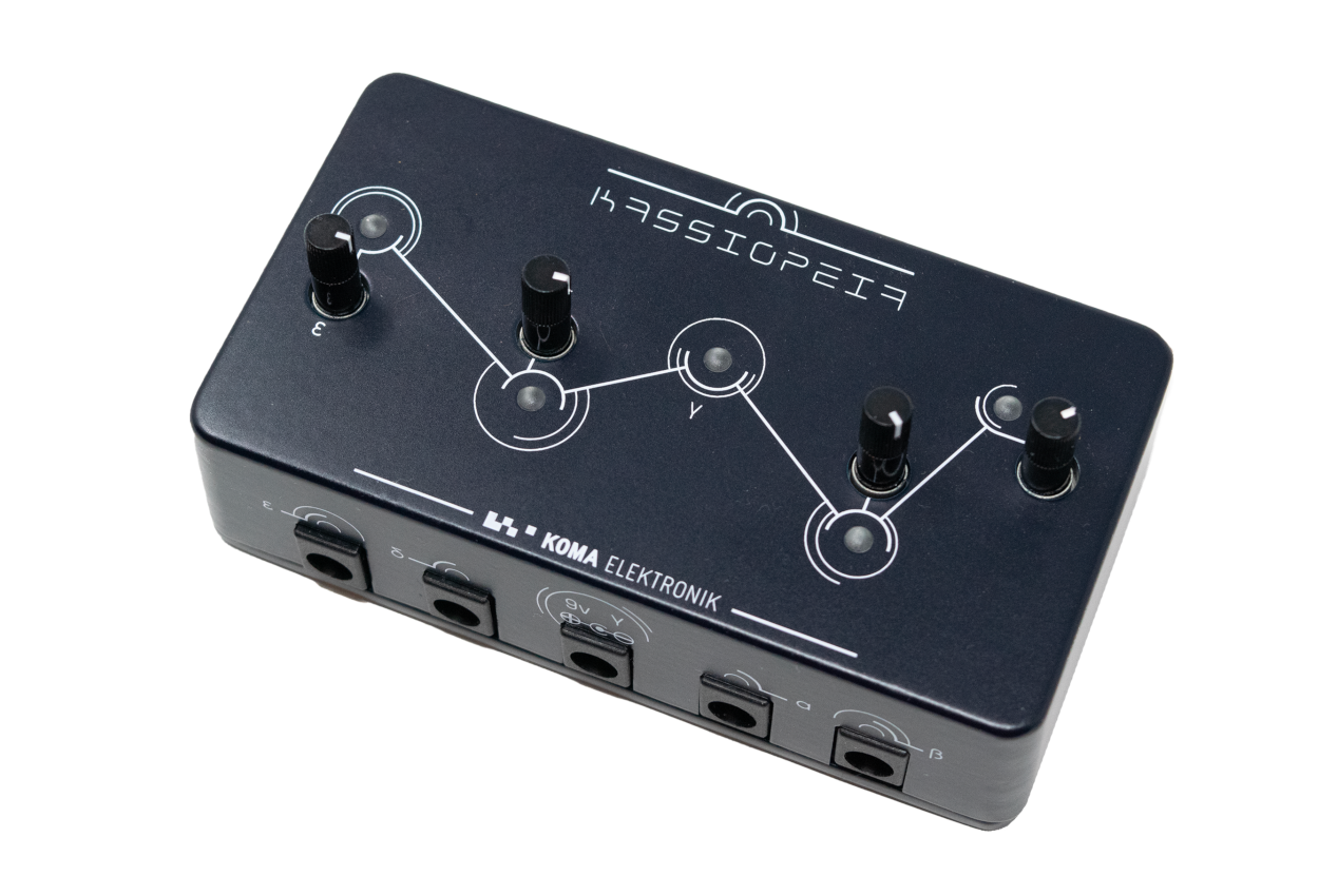 A black electronic music effects unit labeled Kassiopeia by Koma Elektronik, featuring five black knobs arranged on a constellation-like pattern and several audio input/output jacks along the front edge.