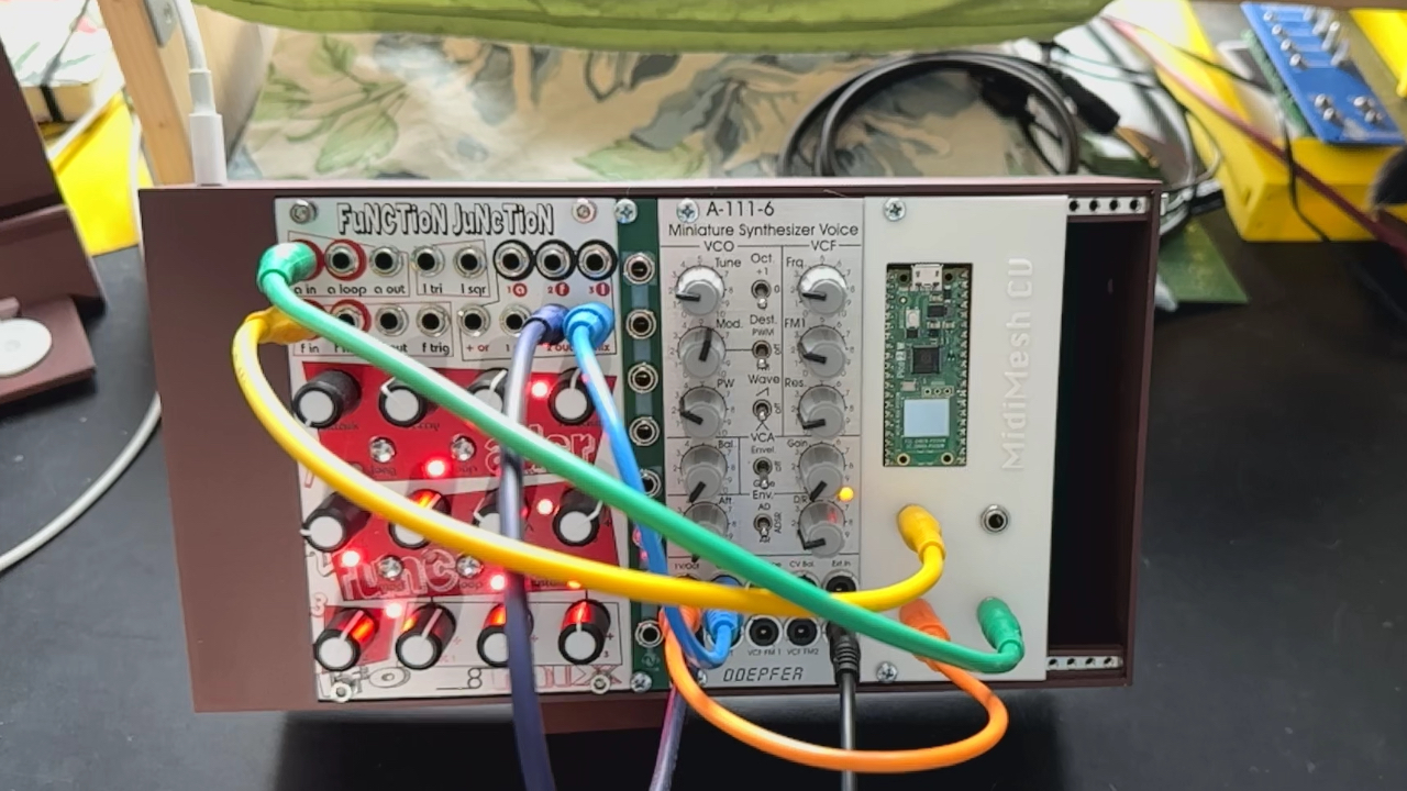 A modular synthesizer setup with various colored patch cables connecting Function Junction, a red Befaco module, an A-111-5 Mini Synthesizer Voice, and a Midi/USB interface on a black tabletop.