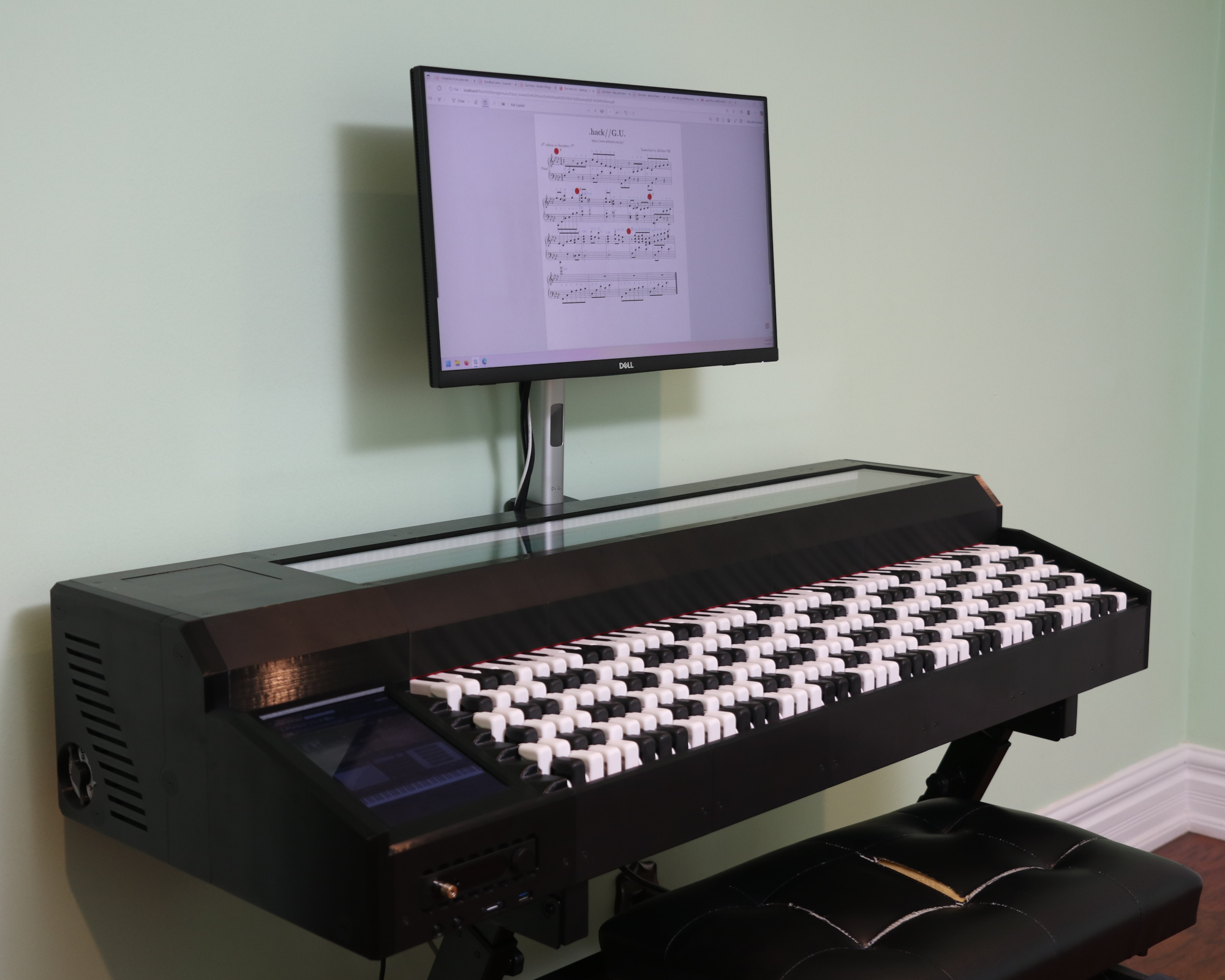 A modern electronic instrument with numerous white and black rectangular keys sits against a green wall, beneath a monitor displaying digital sheet music.