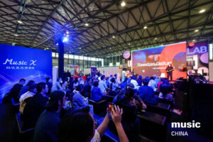 A crowd sits facing a stage at Music Chna watching a presentation on Hawaiian guitar. Bright lights illuminate the stage, and music CHINA is displayed in the bottom right corner.