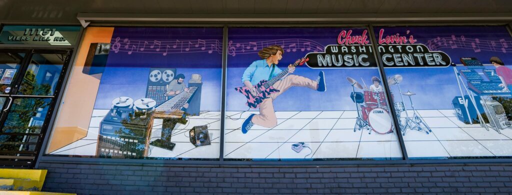 A colorful mural on a storefront shows animated musicians playing guitar, drums, and keyboard, with musical notes and music equipment, advertising Chuck Levins Washington Music Center.