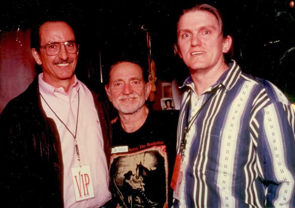 Bruce Crockett, Ensoniq founder, Willer Nelson and Roy Elkins pose together, smiling for the camera. The man in the middle has a beard and wears a black graphic T-shirt, while the men on either side wear collared shirts and have VIP badges hanging from their necks.