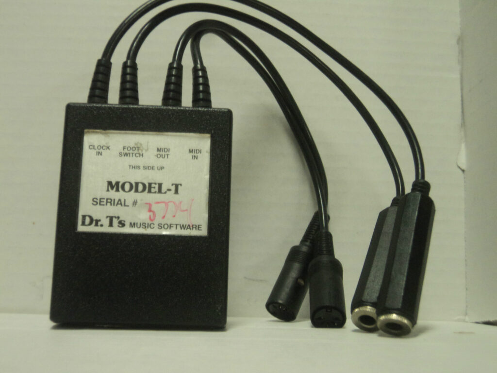 A black rectangular electronic device labeled MODEL-T from Dr. Ts Music Software has attached cables ending in MIDI and audio jacks, placed against a plain white background.