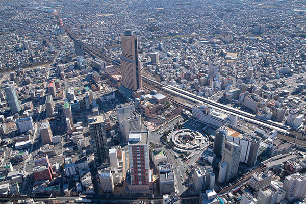 Aerial view of a densely packed city with numerous tall buildings, a prominent roundabout, and elevated highways running through the urban landscape.
