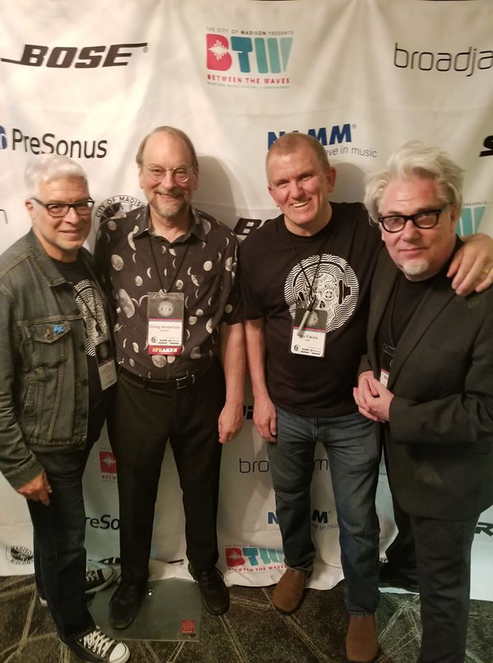 Four men stand together smiling in front of a step-and-repeat banner with logos including Bose, PreSonus, and NAMM. They are dressed casually and wearing event badges around their necks.