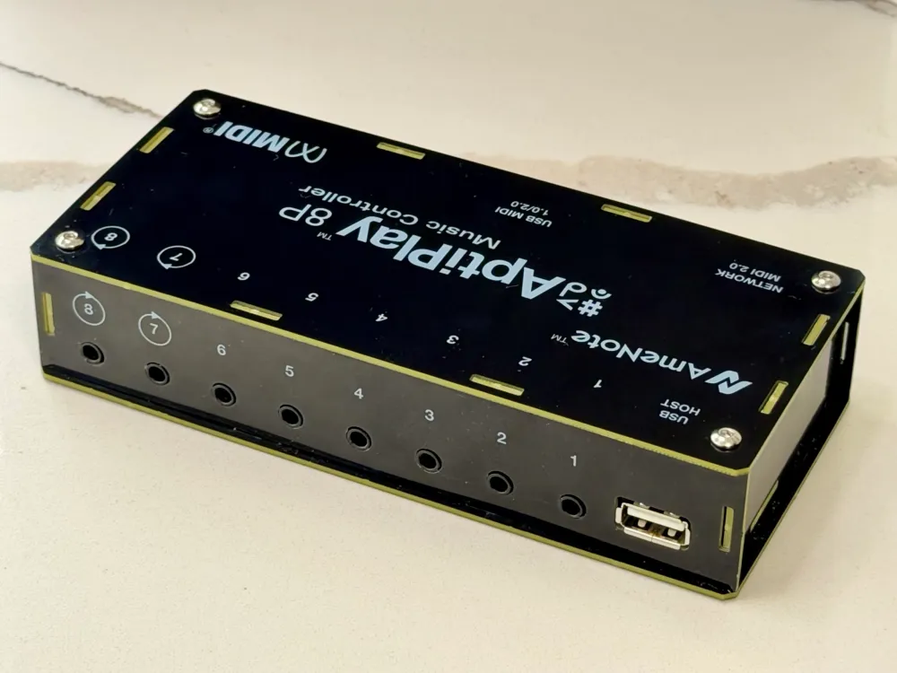 A black Nemeotone Adaptilay 8P music controller device with several numbered input/output ports, a USB port, and a box-like design, resting on a light-colored surface.