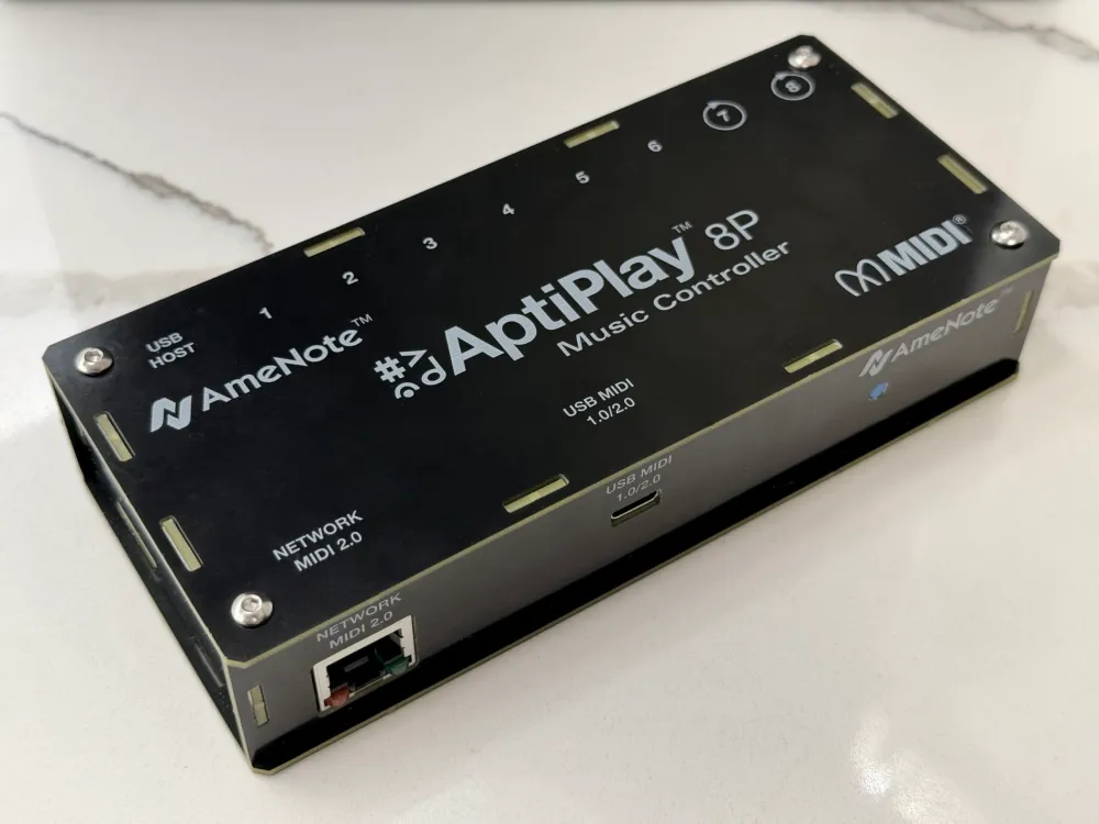 A black rectangular 8-port MIDI music controller labeled AptiPlay 8P by AmeNote, with multiple USB and network ports, resting on a white marble surface.