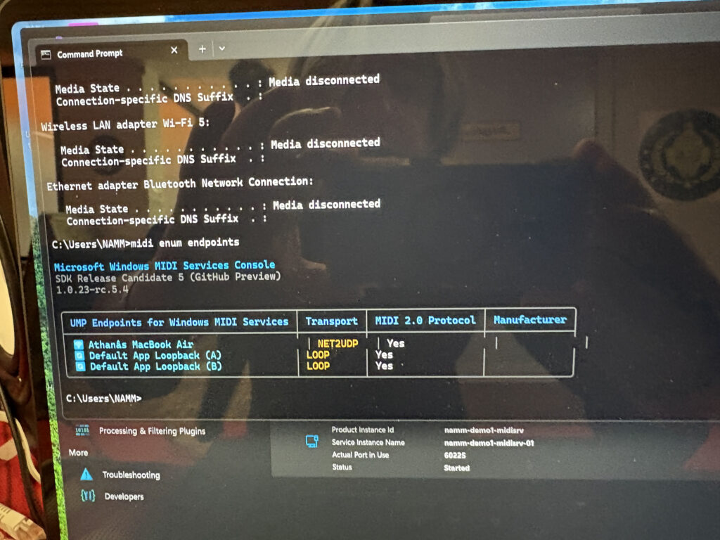 A computer screen displays a Command Prompt window showing network adapter statuses as Media disconnected and a list of MIDI endpoints under Microsoft Windows MIDI Services Console. Other software details are visible below.
