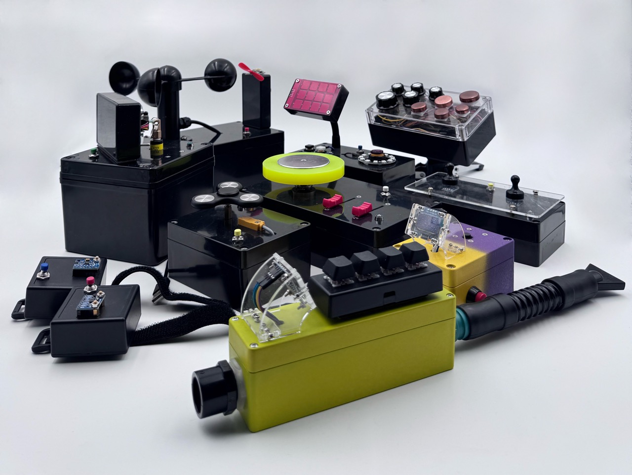 A collection of colorful, uniquely designed electronic devices with various buttons, knobs, levers, and switches arranged on a white background. The devices have a retro, experimental, and futuristic appearance.