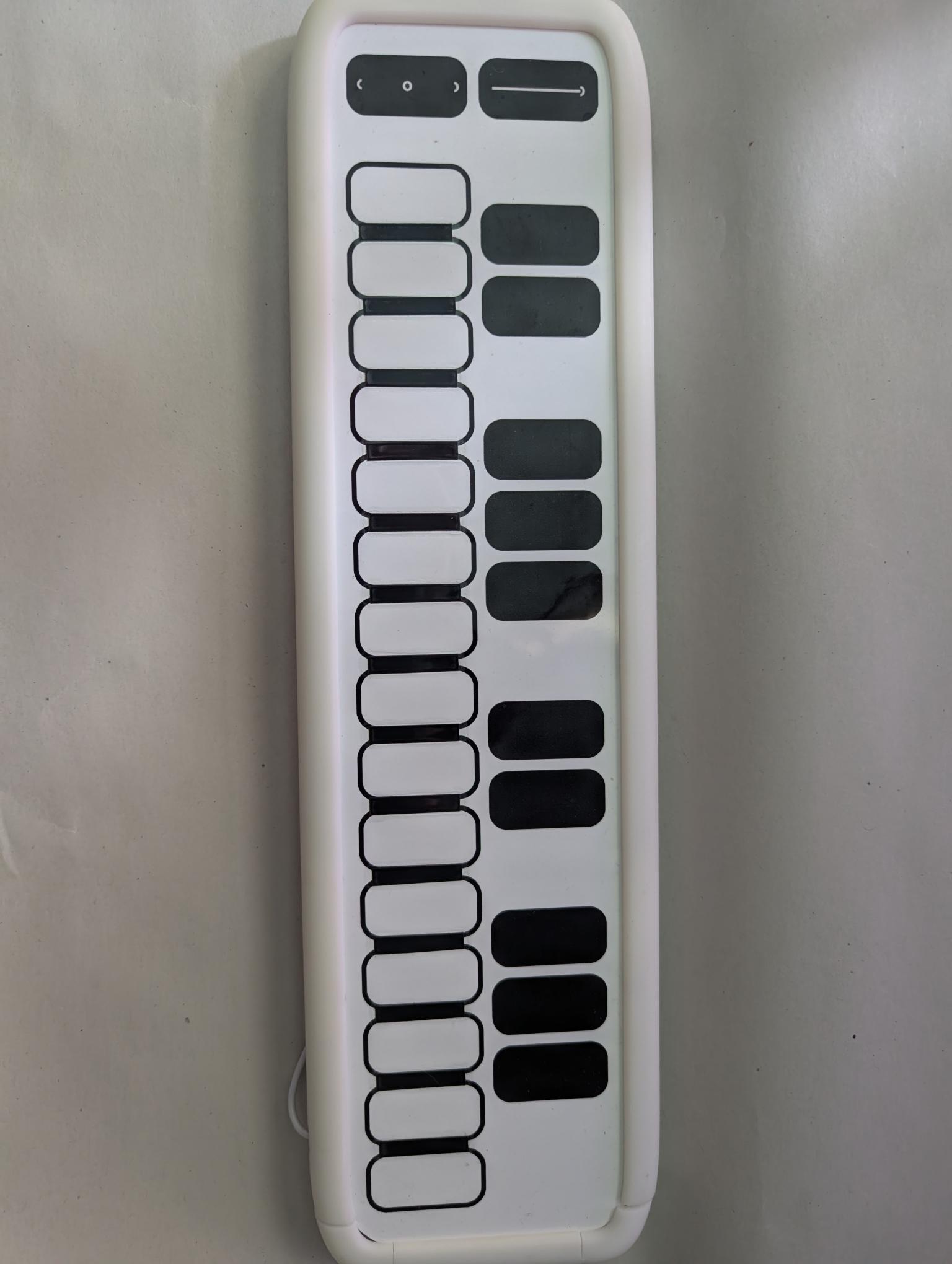 A white electronic keyboard with rectangular black and white keys arranged in two columns, set against a plain light background. The device has a display and buttons at the top.