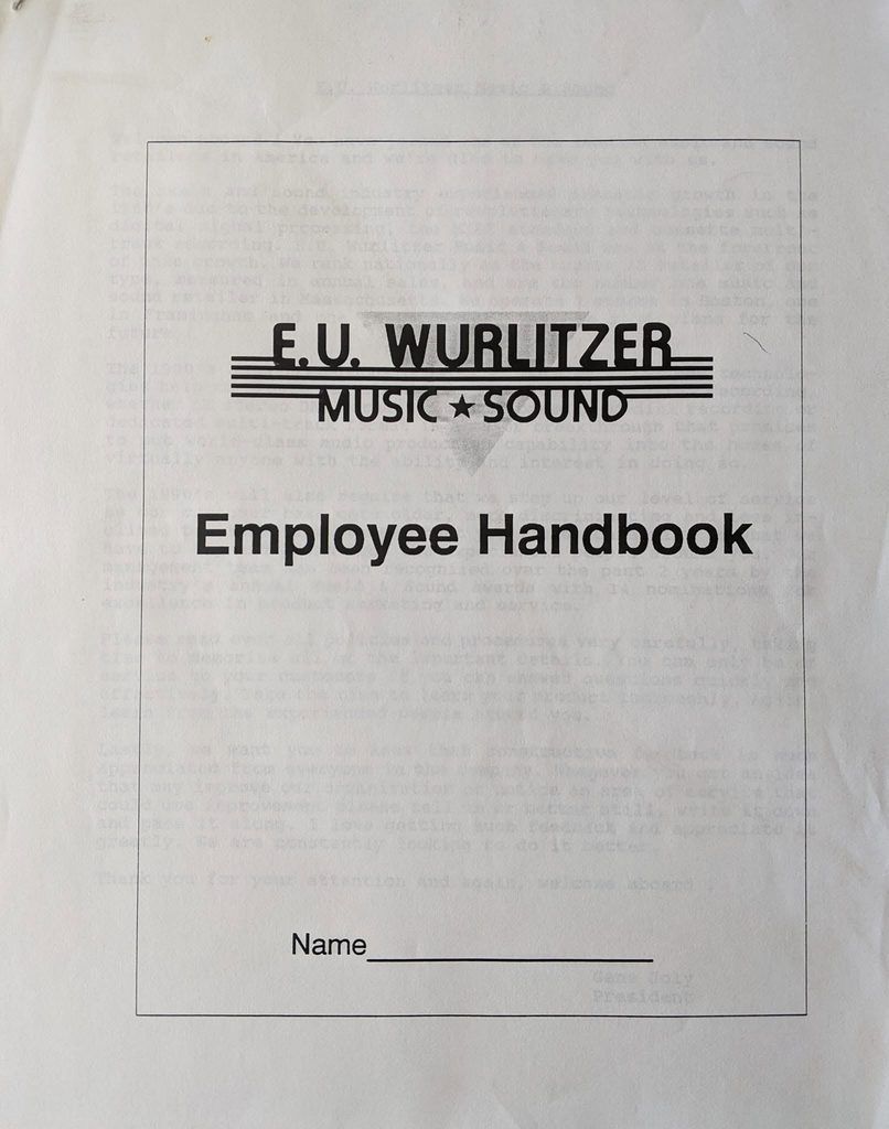 Cover of the E.U. Wurlitzer Music Sound Employee Handbook, with a blank line for the employees name at the bottom. The page is slightly wrinkled and has faint text visible underneath.