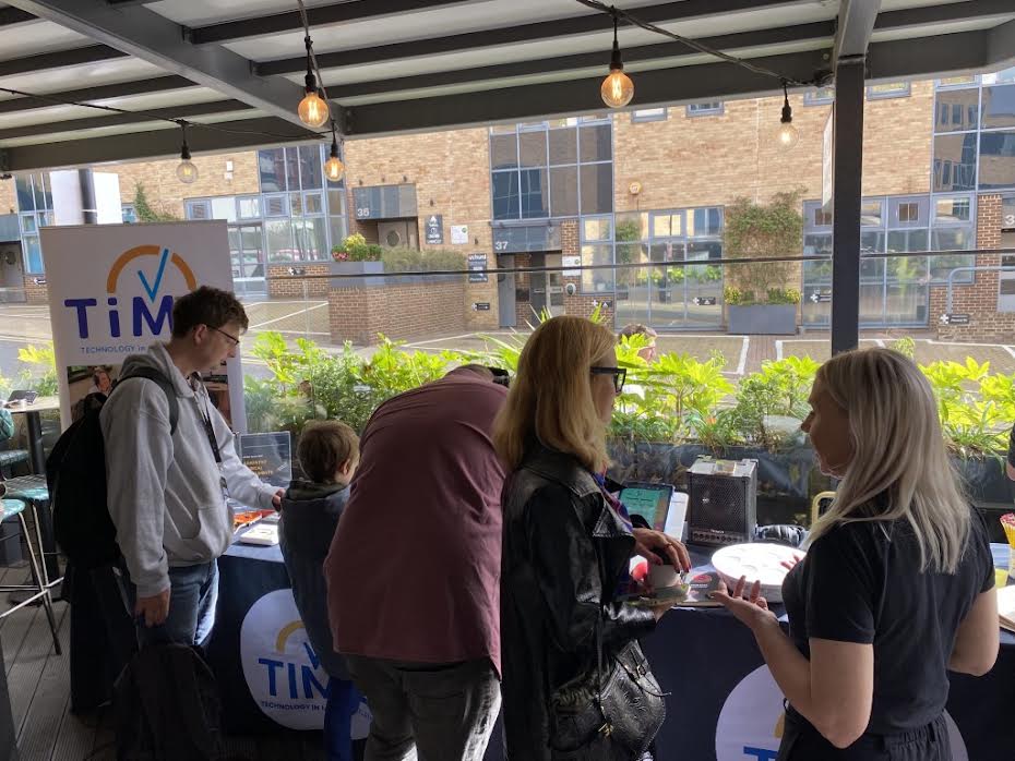 A group of people standing at a TiM Technology in Motion information booth during an outdoor event.