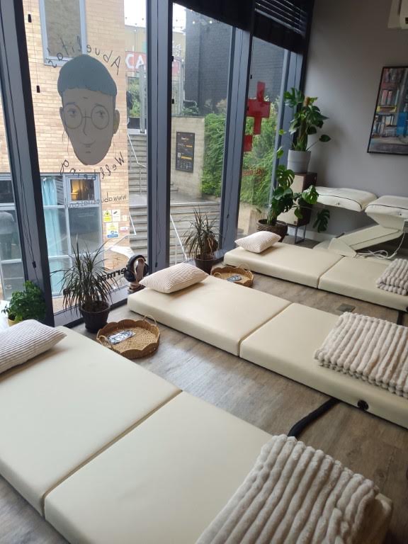 Three cream-colored massage mats laid out on a wooden floor in a studio with large windows.